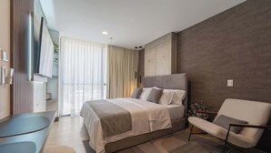 A modern bedroom with a bed, a chair, a desk, and a large window with curtains. - RM 309 | Perfect Studio | Luxury Amenities | Pool (Cali)