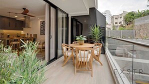 A modern apartment with a balcony, a dining area with wooden furniture, and a view of the cityscape.
