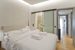A modern hotel room with a large bed, a bedside table, and a bathroom visible through a glass door. - Stylish Ilisia Stay Luxury Fully Reno 2BR, 2BA Apt (Athens)