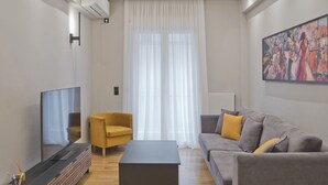 A modern living room with a flat-screen TV, a yellow armchair, a grey sofa with yellow cushions, and a large painting on the wall. - Stylish Ilisia Stay Luxury Fully Reno 2BR, 2BA Apt (Athens)