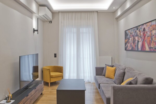 A modern living room with a flat-screen TV, a yellow armchair, a grey sofa with yellow cushions, and a large painting on the wall. - Stylish Ilisia Stay Luxury Fully Reno 2BR, 2BA Apt (Athens)