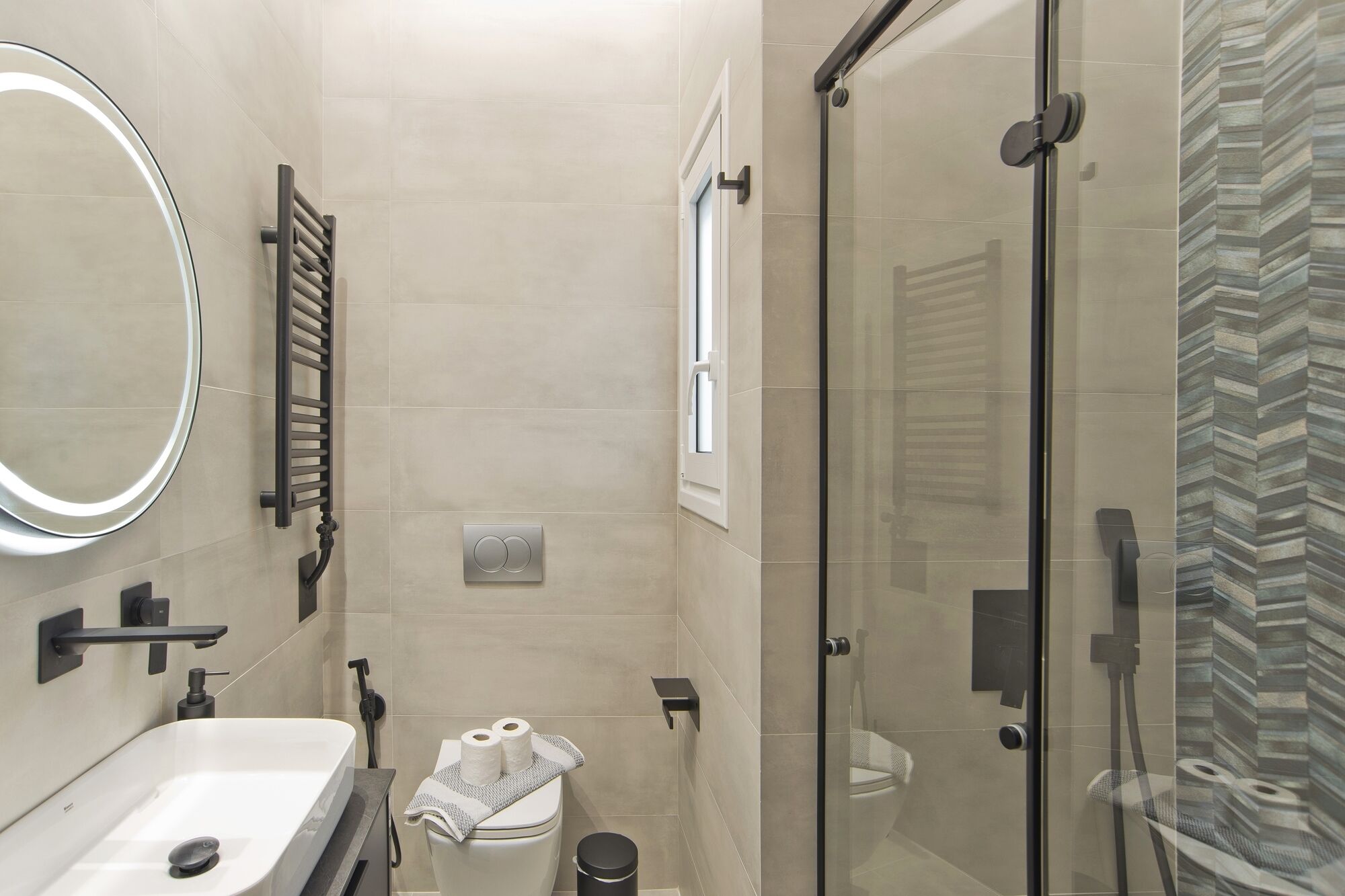 Un baño moderno con cabina de ducha de vidrio, inodoro con toalla y lavamanos con espejo.