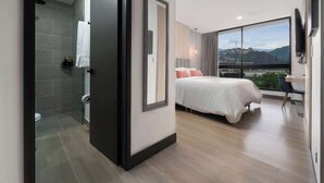 A modern hotel room with a large bed, a desk, and a view of the cityscape.