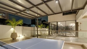 An indoor recreational area with a ping pong table, glass walls, and a ceiling with exposed beams.