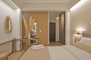 A modern hotel room with a bed, a desk with chairs, a mirror, and a door.