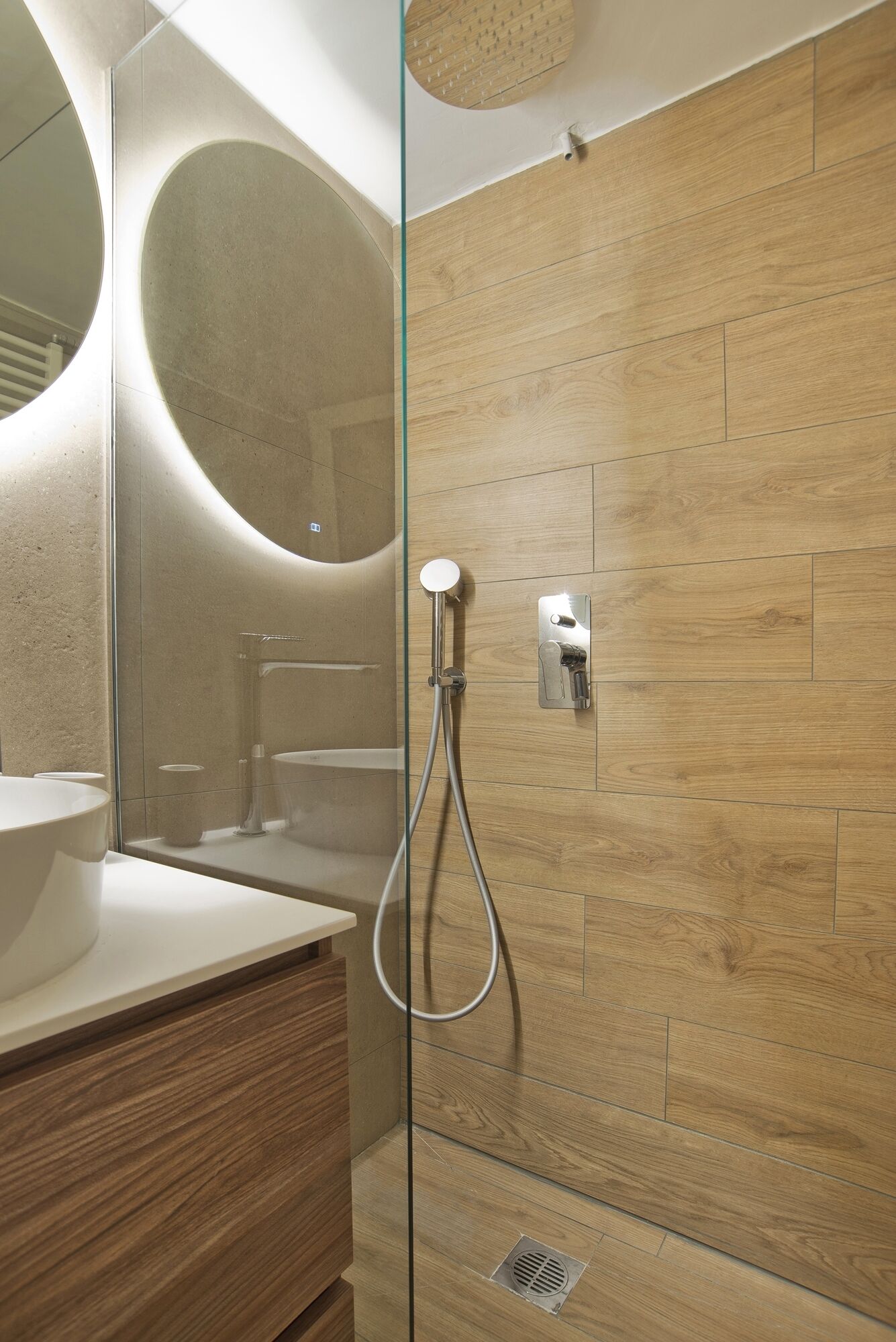 Un baño moderno con ducha de vidrio, un espejo grande y un tocador de madera.