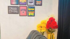 Une pièce avec un canapé noir, un mur décoré de posters inspirants et un vase contenant des fleurs jaunes et rouges.