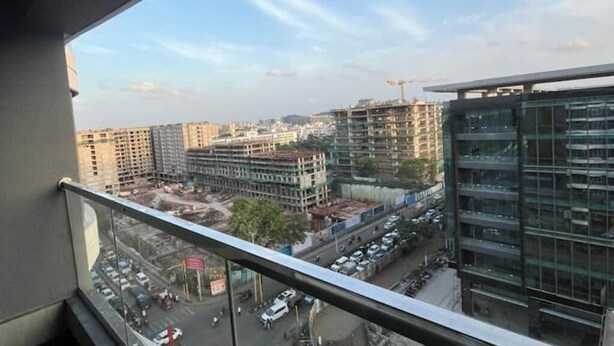 Une vue depuis un balcon donnant sur un paysage urbain avec de nombreux immeubles de grande hauteur, dont certains sont en construction, et un ciel dégagé.