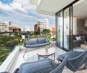 A balcony with a sofa, chairs, and a table, overlooking a cityscape. - RM703 | High-Rise Condo| Pool, Gym & Free Parking⭐ (Cali)