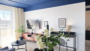 Un salon moderne comprenant un téléviseur à écran plat, une table basse, un canapé, une table d’appoint et un bureau avec une lampe.