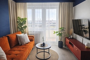 A modern living room with a sofa, coffee table, TV, and potted plants.