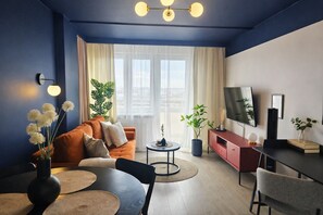 A modern living room with a sofa, coffee table, TV, and plants. - Apartament Gwarek - by Kairos Apartments (Katowice)