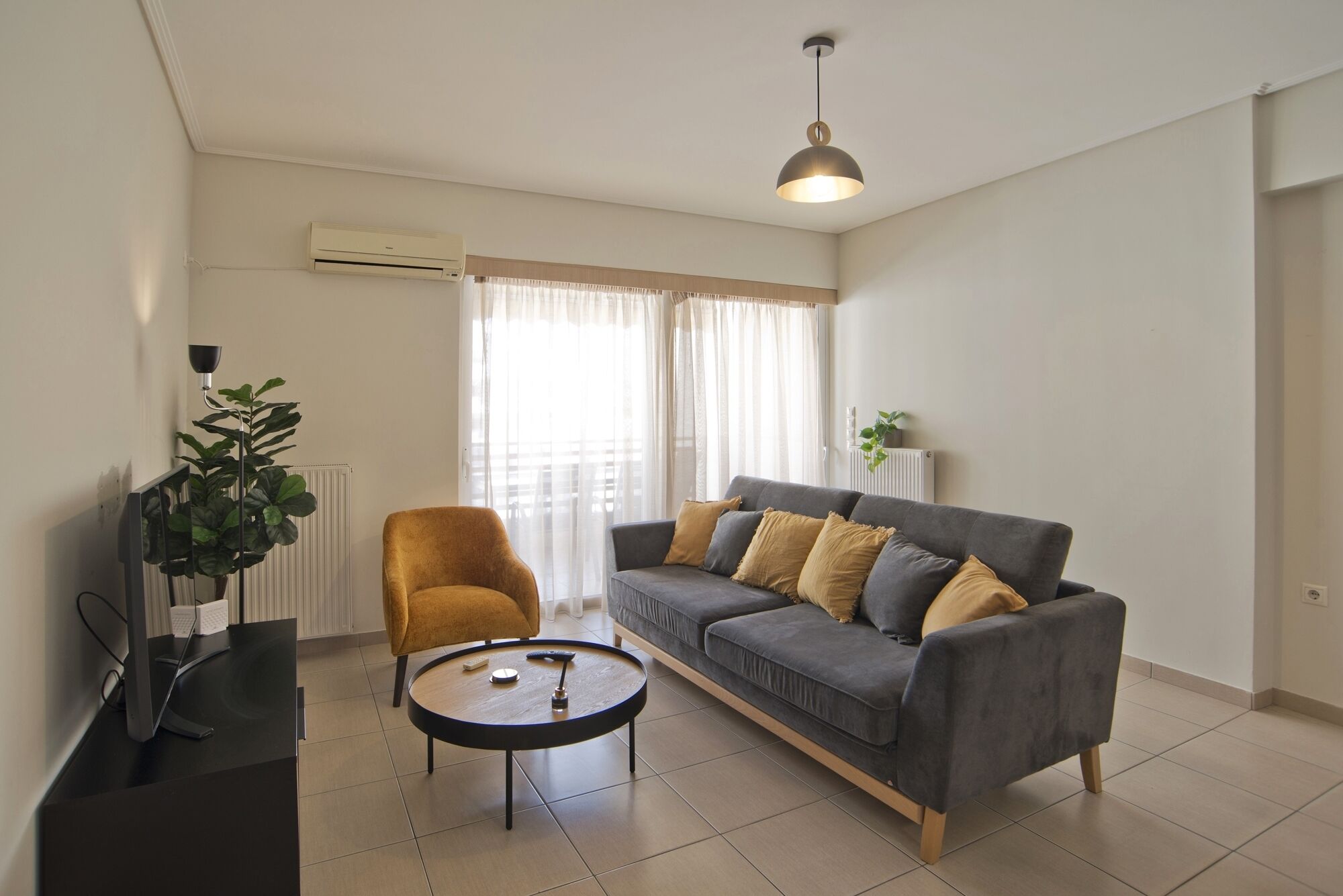A modern living room with a grey sofa, a round coffee table, a yellow armchair, and a floor lamp.