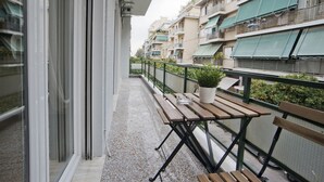 A balcony with a wooden table and chairs, a potted plant, and a railing.