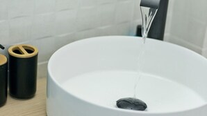 A modern bathroom with a round white sink, a black faucet, and a glass container on the counter.