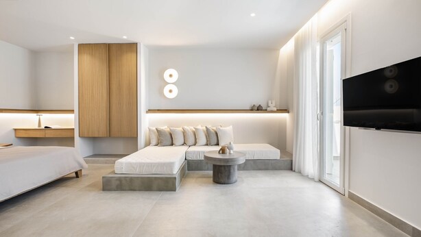 Een moderne hotelkamer met een bed, een bank en een aan de muur bevestigde televisie.