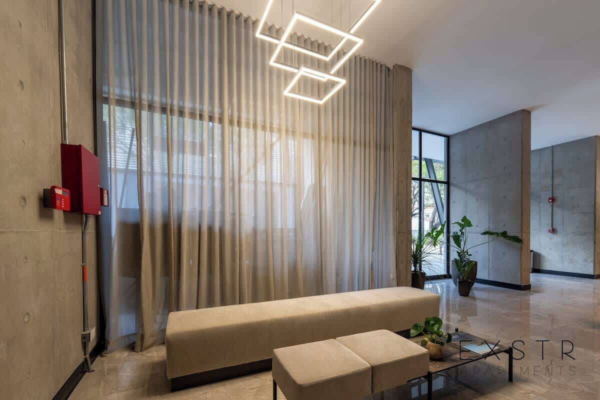 Un soggiorno moderno con un divano, poggiapiedi e una lampada geometrica.
