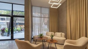A modern living room with a sofa, two armchairs, and a coffee table. There are large windows with curtains, a view of the street outside, and a geometric ceiling light fixture. - RM902| LuxeHigh- Hideaway – Pool, Sauna & Security (Cali)