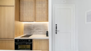 A modern kitchen with wooden cabinets, a built-in stove, and a white door. - Kythnos Blue - Suite 4 Luxurious, Sea Front (Kythnos)