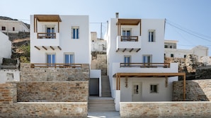 A modern two-story building with a stone facade, wooden balconies, and a staircase leading to the entrance. - Kythnos Blue - Suite 4 Luxurious, Sea Front (Kythnos)