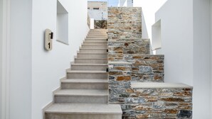 A staircase with a stone wall on one side and a white wall on the other, leading to a higher level. - Kythnos Blue - Suite 4 Luxurious, Sea Front (Kythnos)