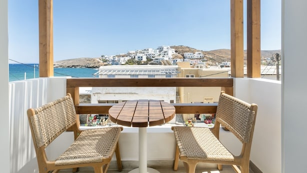 A balcony with wicker chairs and a small table, overlooking a coastal town with white buildings and a clear blue sky. - Kythnos Blue - Suite 4 Luxurious, Sea Front (Kythnos)
