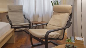 Ein Hotelzimmer mit einem Bett, zwei Stühlen, einem kleinen Tisch mit Kerzen, einem Fernseher und einem Fenster mit Vorhängen.