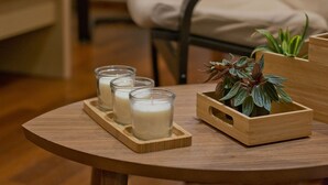 Ein runder Holztisch mit drei Kerzenhaltern aus Glas und einem Pflanzgefäß aus Holz, in dem eine Pflanze steht.