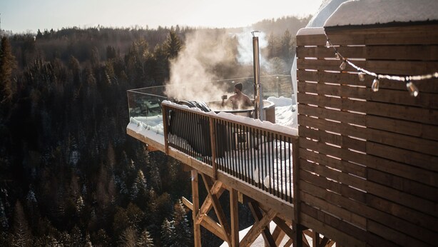 Una terraza de madera con un jacuzzi rodeado de árboles cubiertos de nieve.