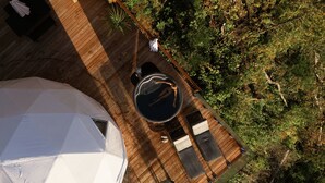 Una terraza de madera con una mesa redonda y sillas, rodeada de abundante vegetación.