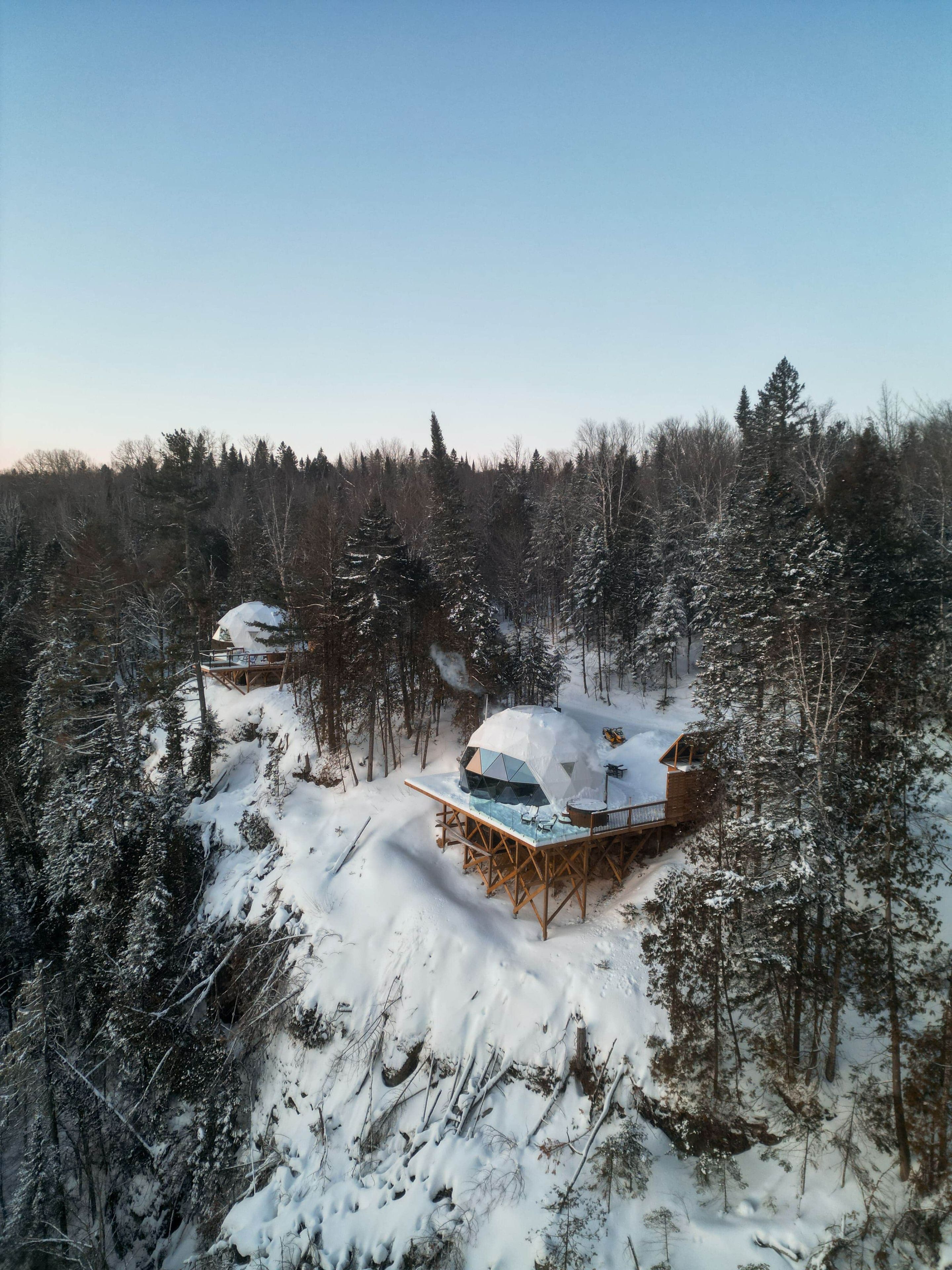 Een besneeuwd bos met een chalet, voorzien van een glazen terras en een houten constructie.
