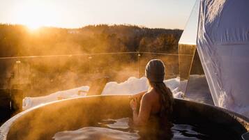 Une personne dans un bain à remous, avec vue sur un paysage enneigé et une tente en arrière-plan.