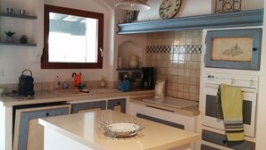 A kitchen with a central island, wooden beams, a window, a clock, and a tiled backsplash.