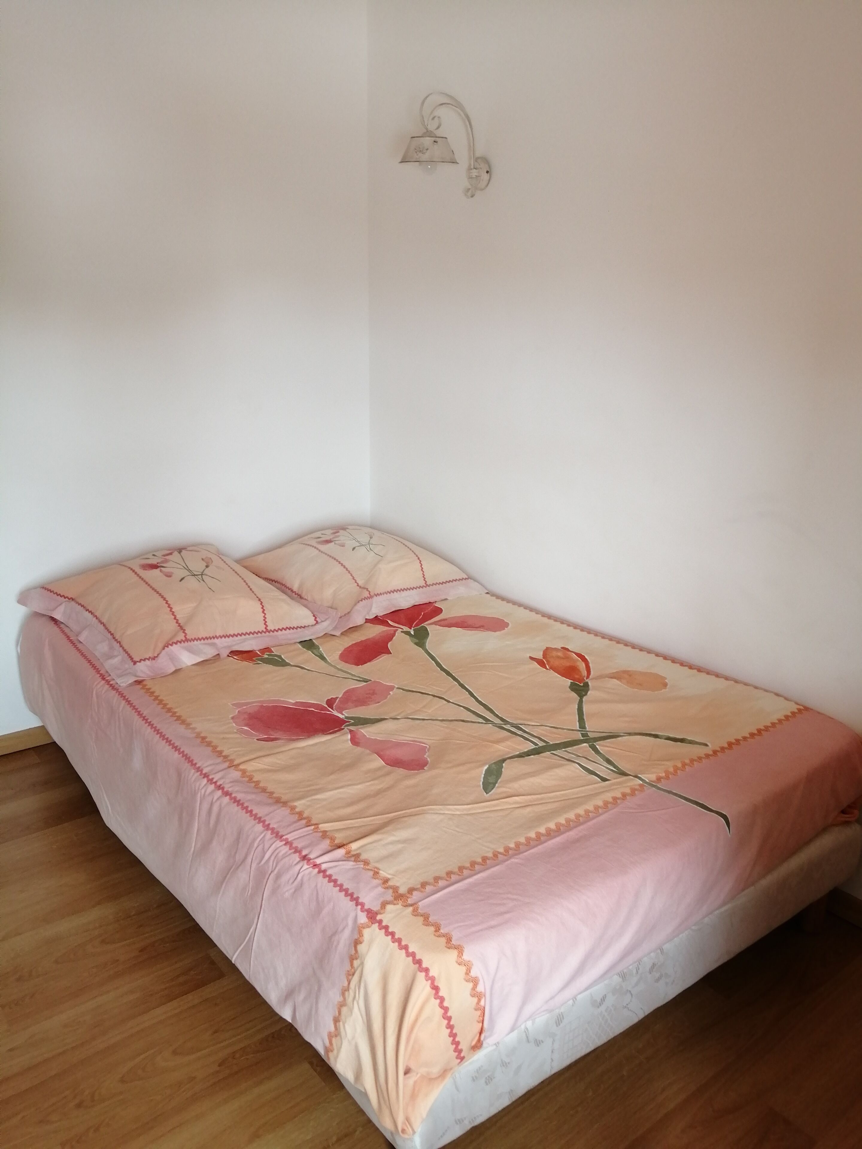 Una cama individual con una colcha estampada y almohadas a juego, una lámpara de pared y suelo de madera.