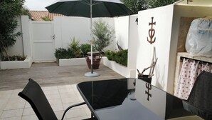 A patio area with a glass table and chairs, a potted plant, and a wall with a decorative anchor symbol.
