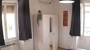 Une pièce comprenant un lit, une armoire, un radiateur et une fenêtre avec des rideaux.