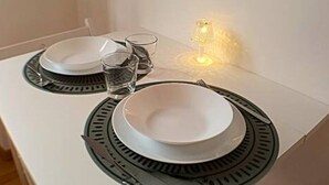 Une table à manger est dressée avec de l’assiette blanche, de l’assiette à bordure noire et des verres transparents, et une petite lampe de table est posée sur la table.