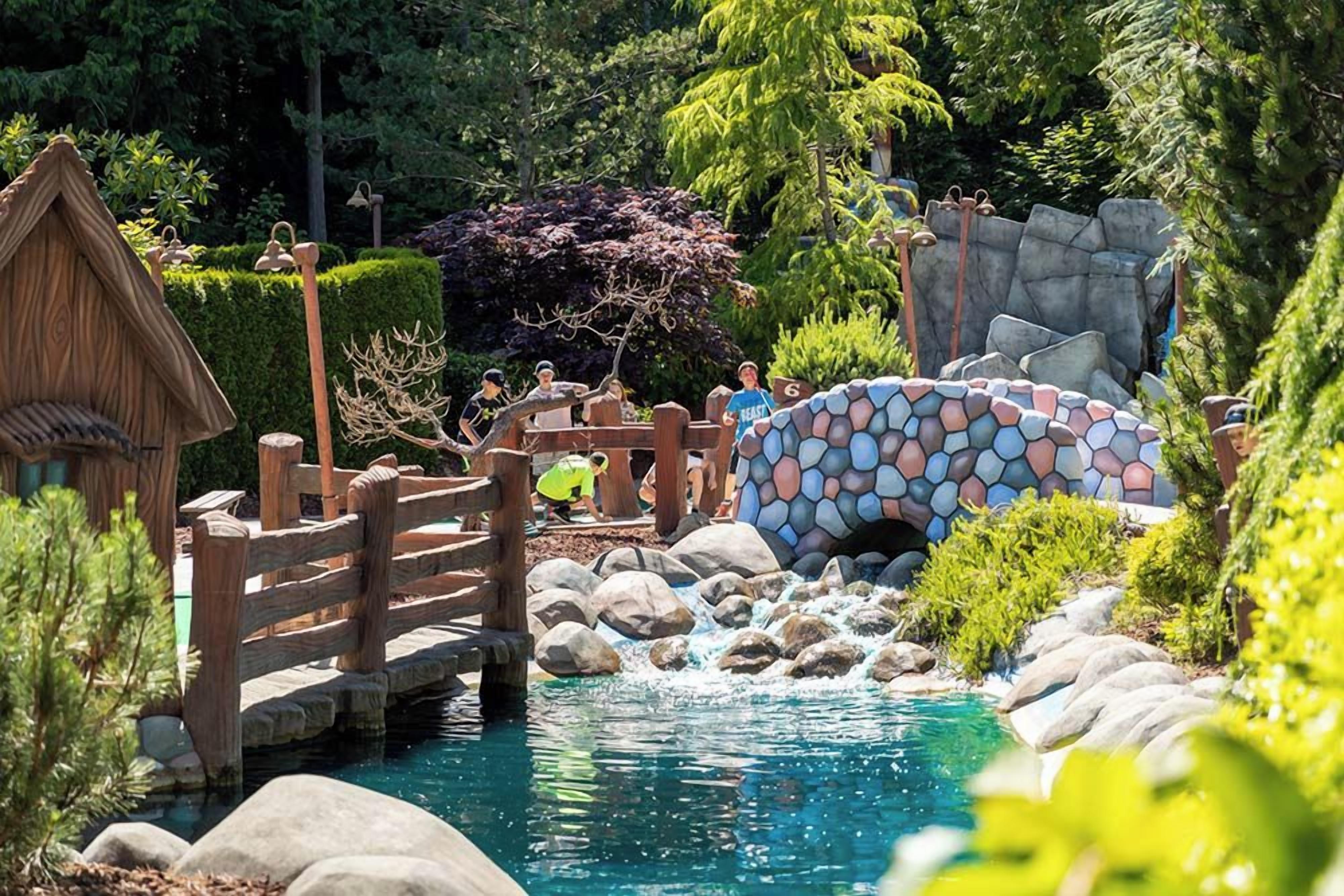 Ein Garten mit einer Holzbrücke, einem Steinkanal und einem kleinen Wasserfall.