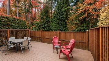 An outdoor deck with a wooden fence, a table with chairs, and red Adirondack chairs.