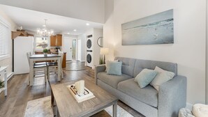 Un soggiorno moderno con un divano grigio, un tavolino in legno e un quadro raffigurante una spiaggia.