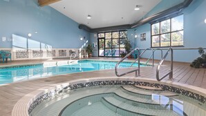Una piscina interna con bordo piastrellato, una stanza luminosa con pareti blu e vista sull'esterno attraverso ampie finestre.