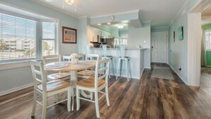 A dining area with a wooden table and chairs, a kitchen in the background, and a hallway leading to another room. - Sea The World- Private Access to Beach! (Carolina Beach)