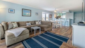 A living room with a sofa, a coffee table, and a rug. There is a dining area with a table and chairs. - Sea The World- Private Access to Beach! (Carolina Beach)