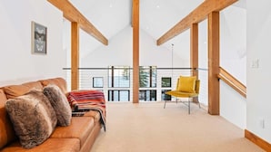 A spacious loft with high ceilings, exposed wooden beams, a leather sofa with plush pillows, a yellow chair, and large windows offering a view of the outdoors.
