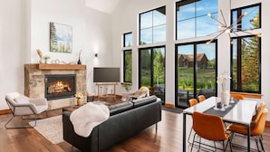 A modern living room with a fireplace, large windows, and a dining area.