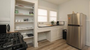 A compact kitchen with white cabinets, a stainless steel refrigerator, a gas stove, and a window providing natural light.