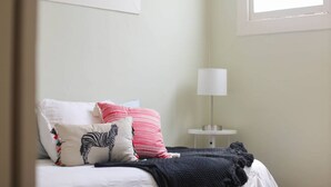 A bedroom with a bed, pillows, a lamp, and a window.