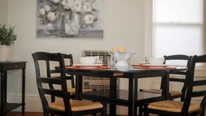 A dining area with a black table, four chairs, a vase with flowers, and a painting on the wall.