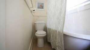 Un baño pequeño y limpio con inodoro, cortina de ducha y un cuadro en la pared.