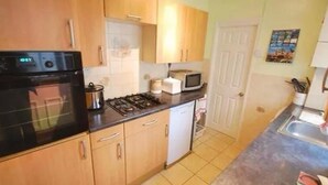 A compact kitchen with a stove, microwave, and a small sink. - Spacious Four-bedroom House With Garden in Wembley (Wembley)